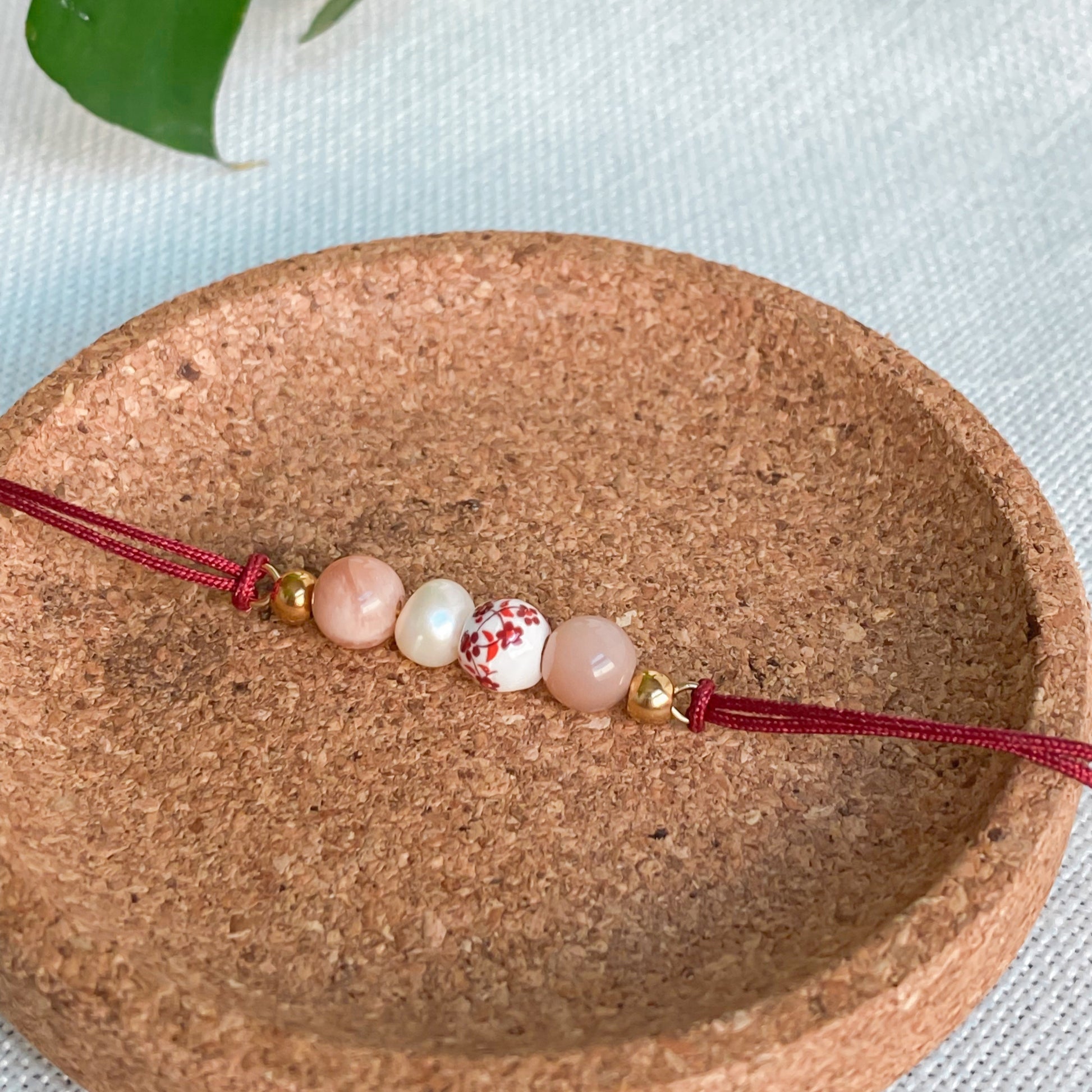 Bracelet cordon rouge en pierres naturelles Éveil présenté sur support naturel en liège, bijou fin et discret pour le quotidien.