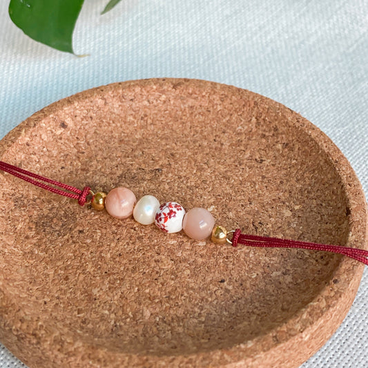 Bracelet cordon rouge en pierres naturelles Éveil présenté sur support naturel en liège, bijou fin et discret pour le quotidien.