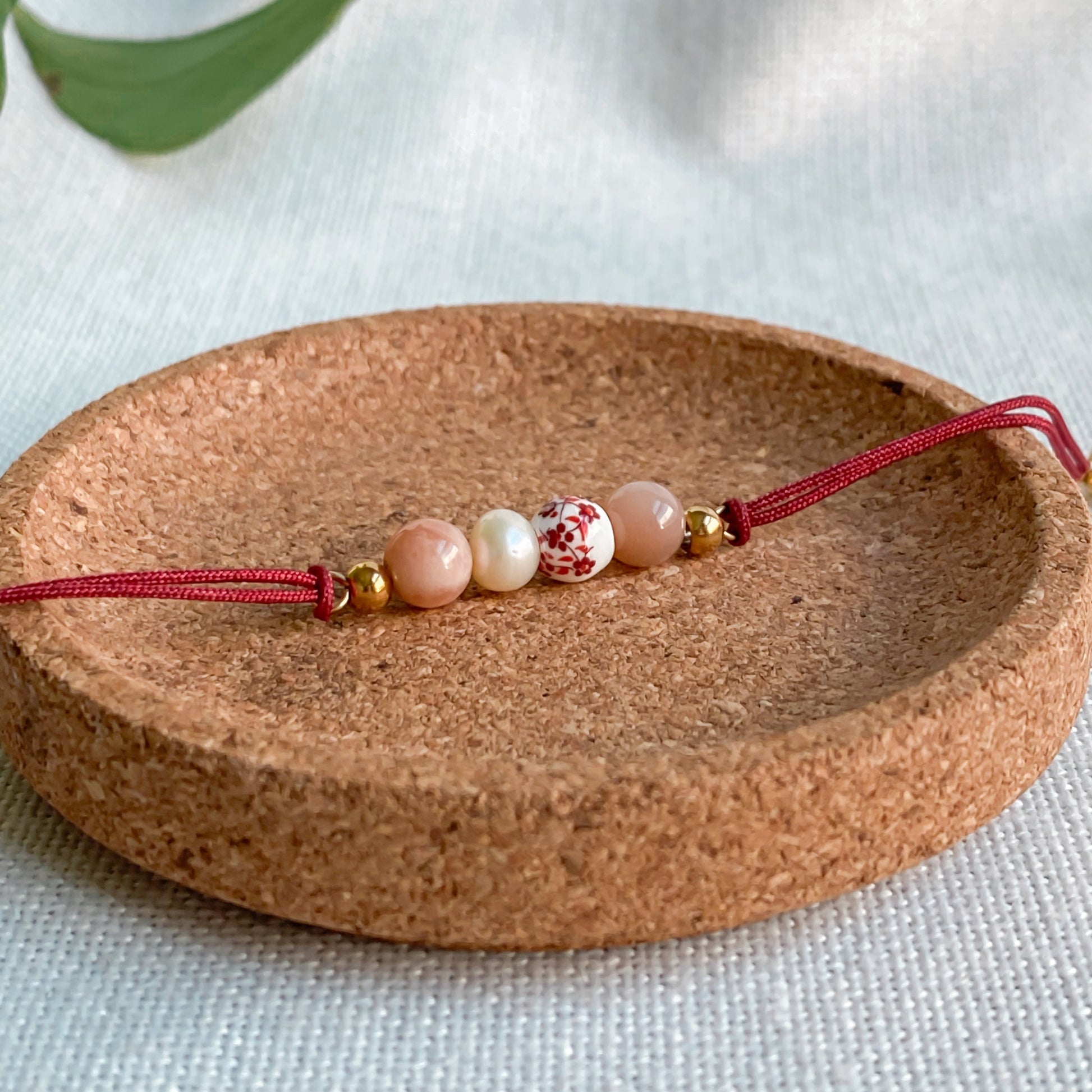 Bracelet cordon rouge ajustable Éveil vu de dessus, bijou artisanal fait main à Montréal avec pierre de soleil, perle d’eau douce et céramique blanche fleurie.