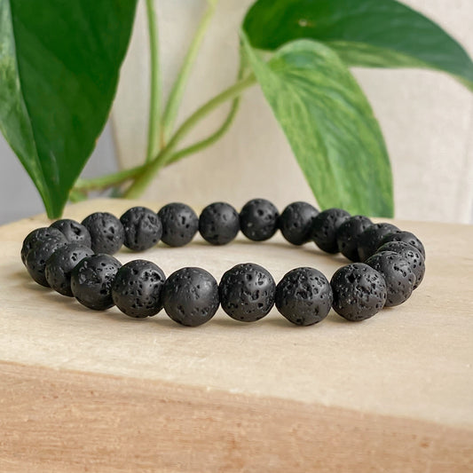 Bracelet diffuseur d'huiles essentielles en pierres de lave noire, vue de face, bijou minimaliste en pierres naturelles, sur fond coton et feuilles.