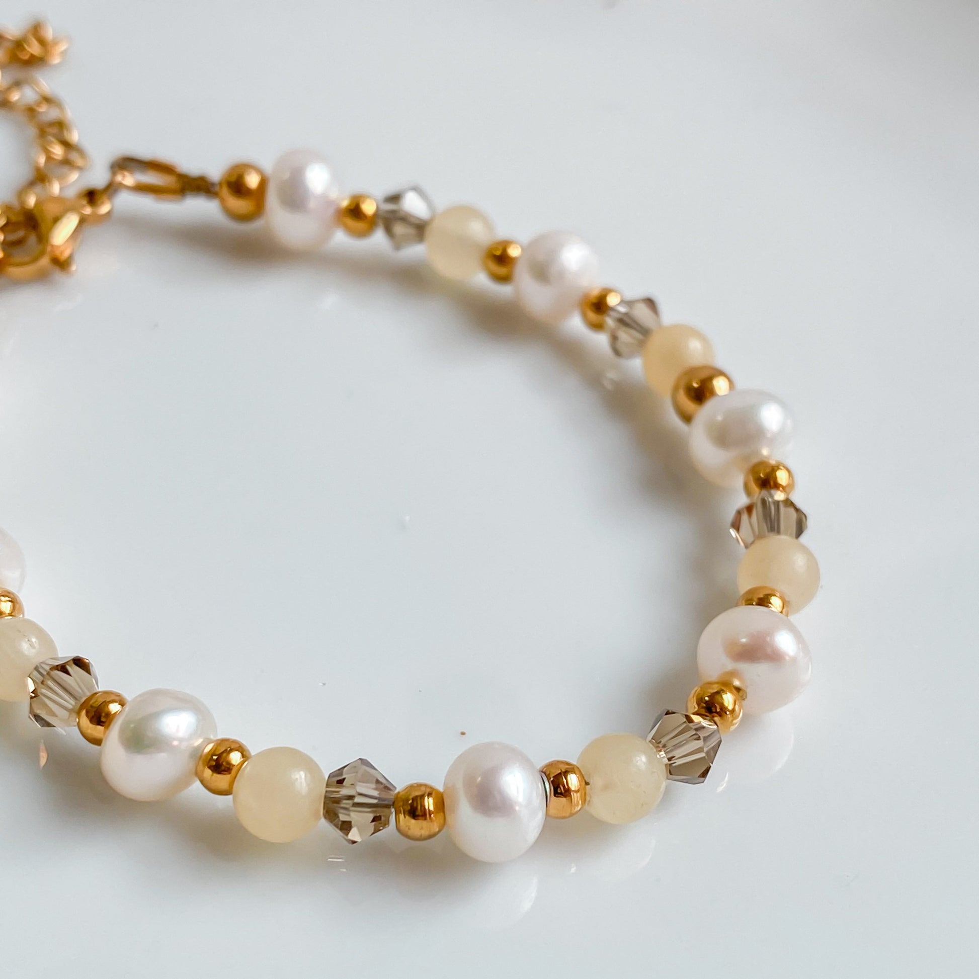 Zoom sur le bracelet doré Théia avec perles d’eau douce et pierres de jade jaune naturelles.