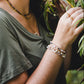 Femme portant le bracelet Hécate en pierres naturelles, bijou artisanal doré avec pierre de soleil, jade blanc, labradorite et perle d’eau douce, dans un décor naturel.