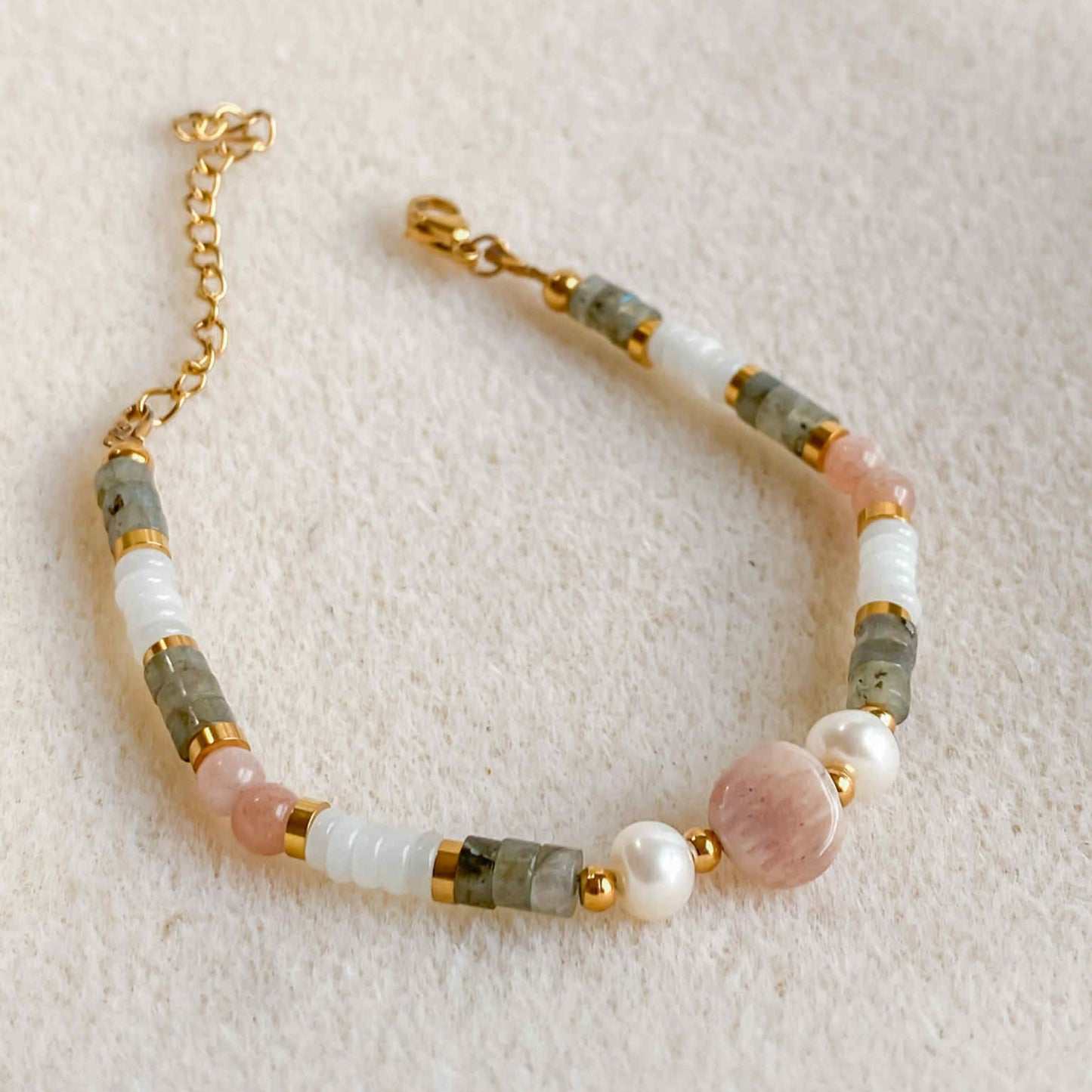 Bracelet Hécate en pierres naturelles avec pierre de soleil, jade blanc, labradorite et perle d’eau douce, sur fond beige.