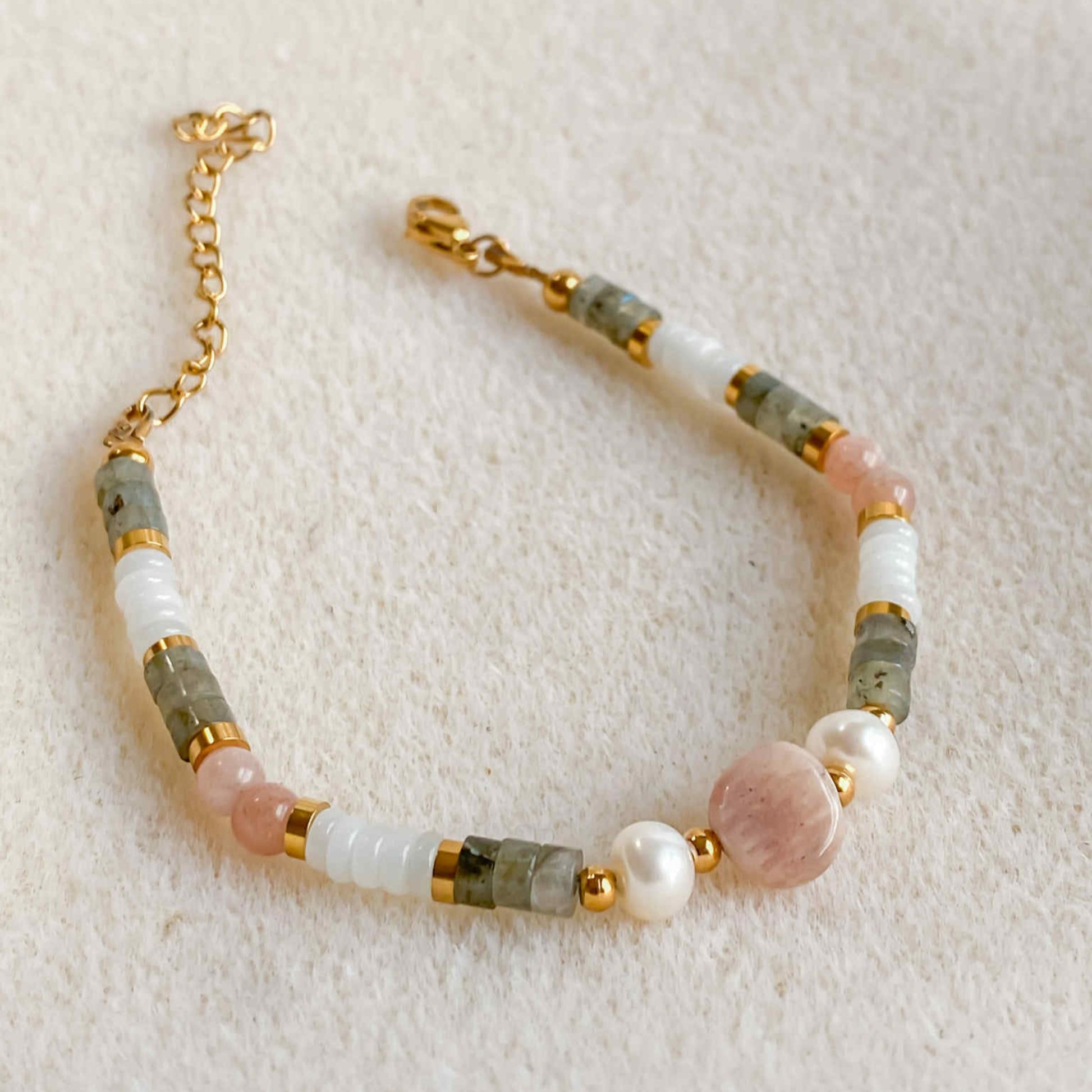 Bracelet Hécate en pierres naturelles avec pierre de soleil, jade blanc, labradorite et perle d’eau douce, sur fond beige.