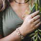 Femme portant plusieurs bracelets en pierres naturelles dont le bracelet Hécate, bijou artisanal doré.
