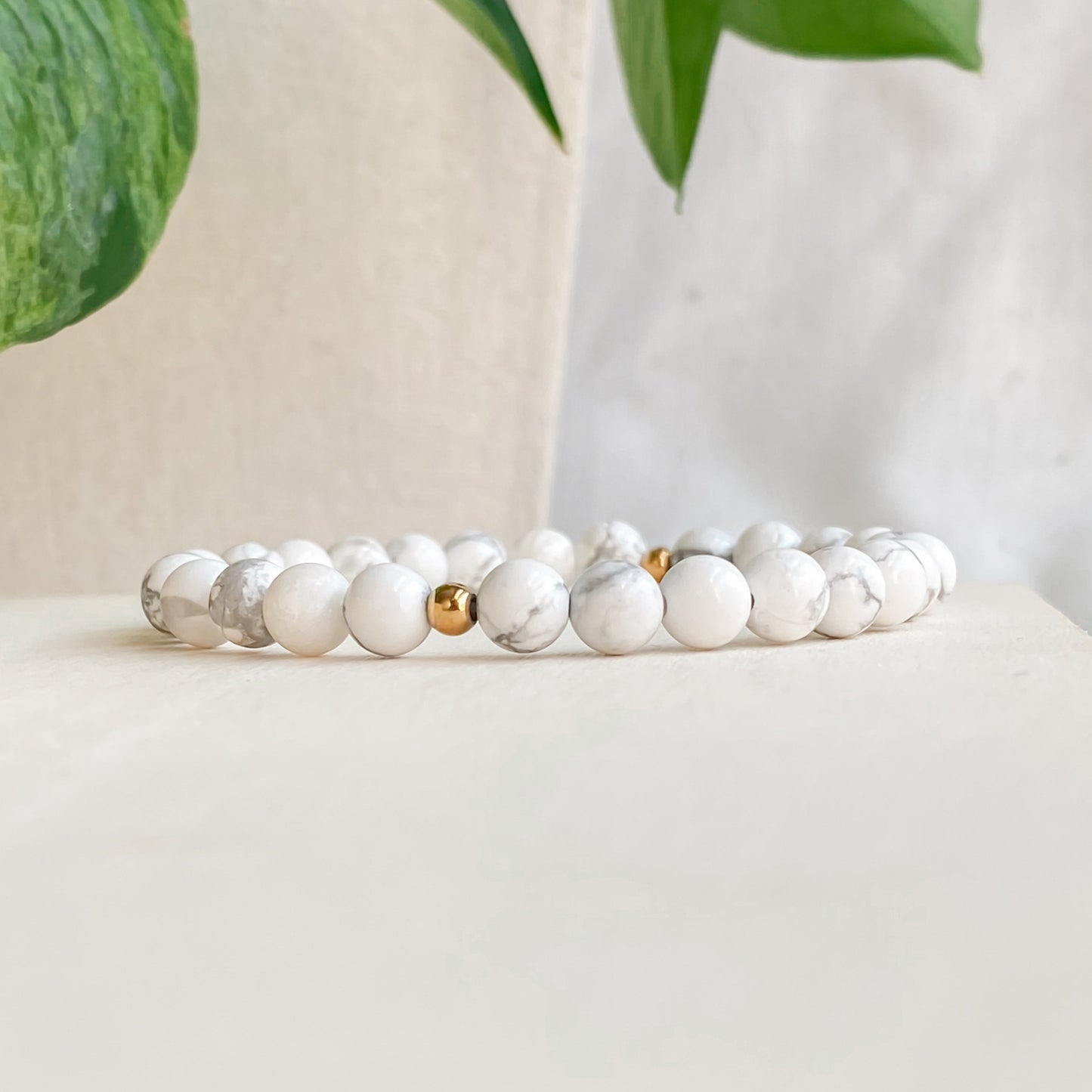 Gros plan du bracelet en howlite 6mm et acier inoxydable doré, vu de côté avec un zoom sur les pierres, posé sur une planche de bois clair avec des plantes autour.