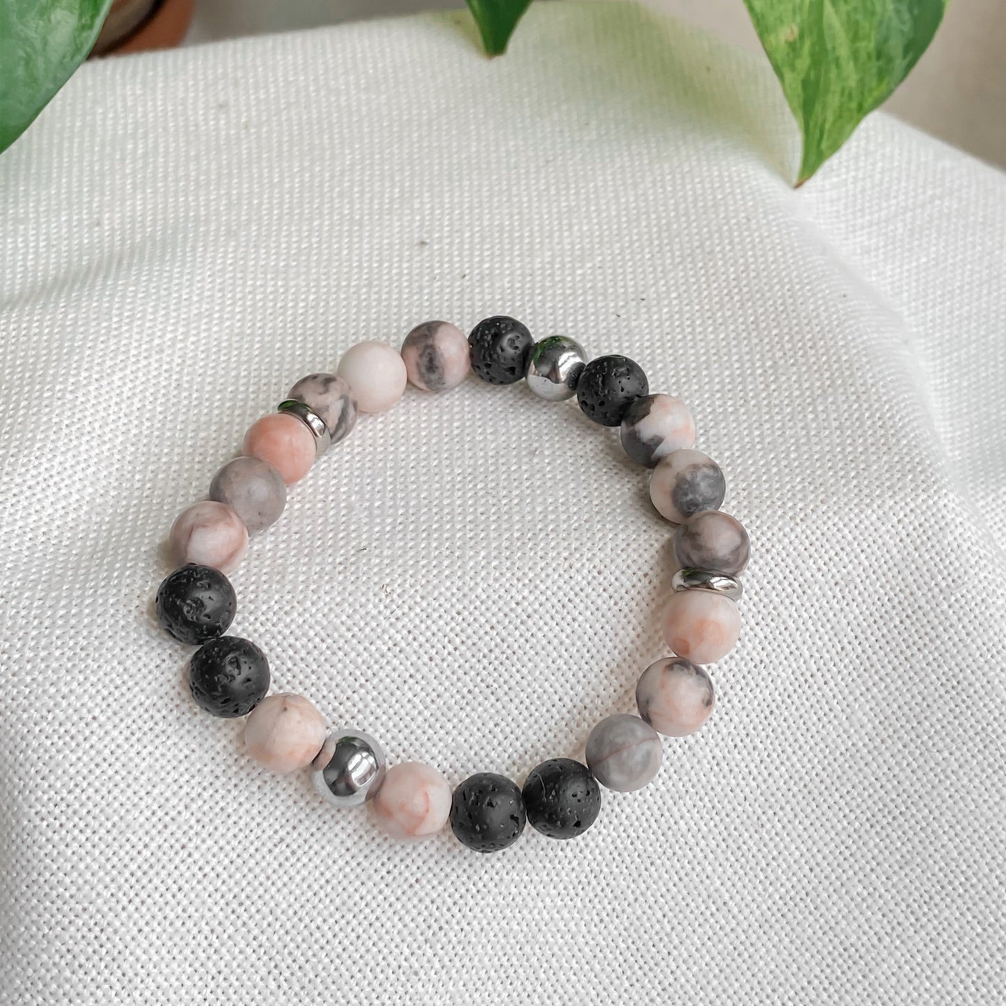 Vue de côté du bracelet Jaspe Zébrée Rose avec Hématite et pierres de lave, posé sur coton, bijou artisanal féminin.