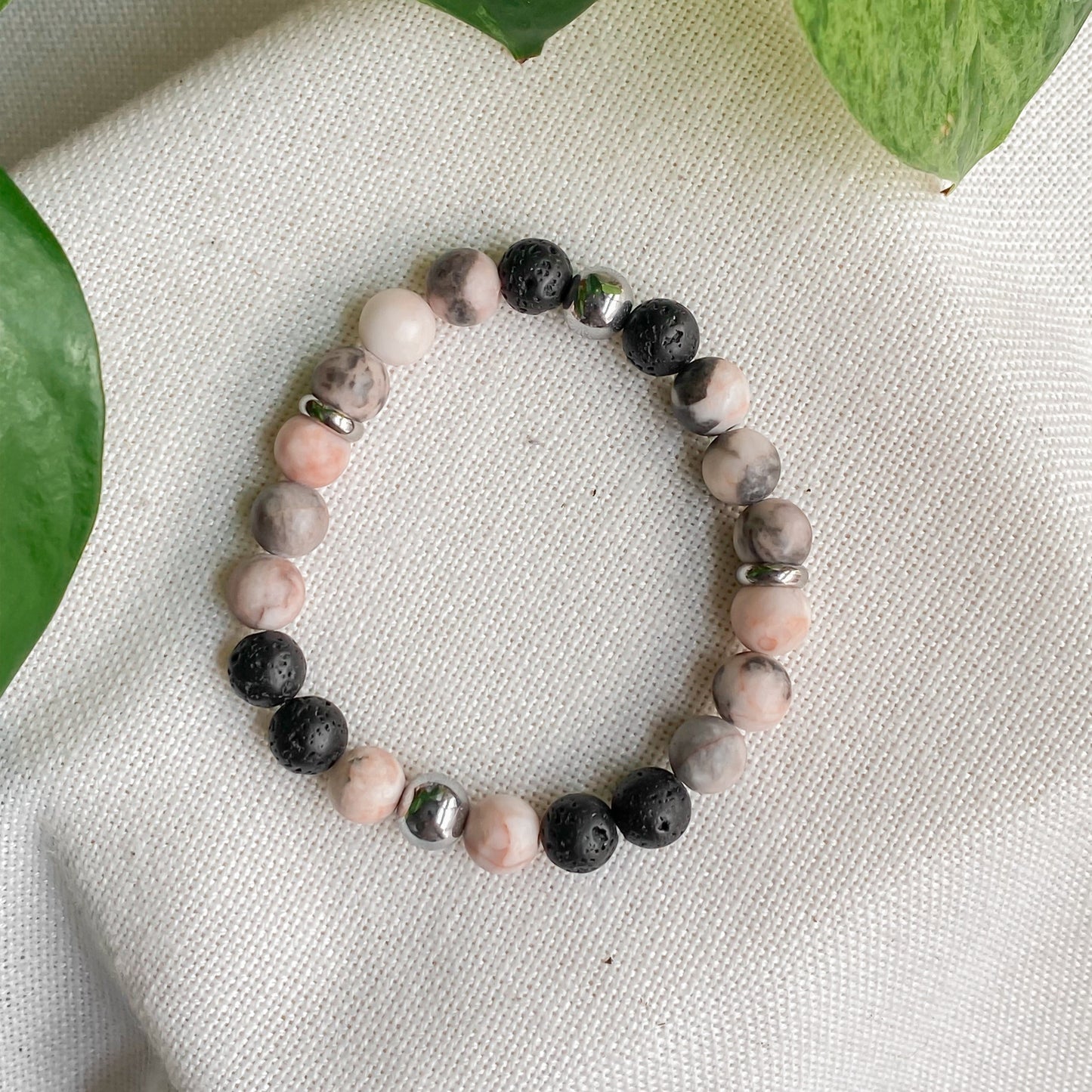 Bracelet en pierres naturelles Jaspe Zébrée Rose et Hématite, vue de haut avec feuilles et support en coton, bijou élégant et féminin