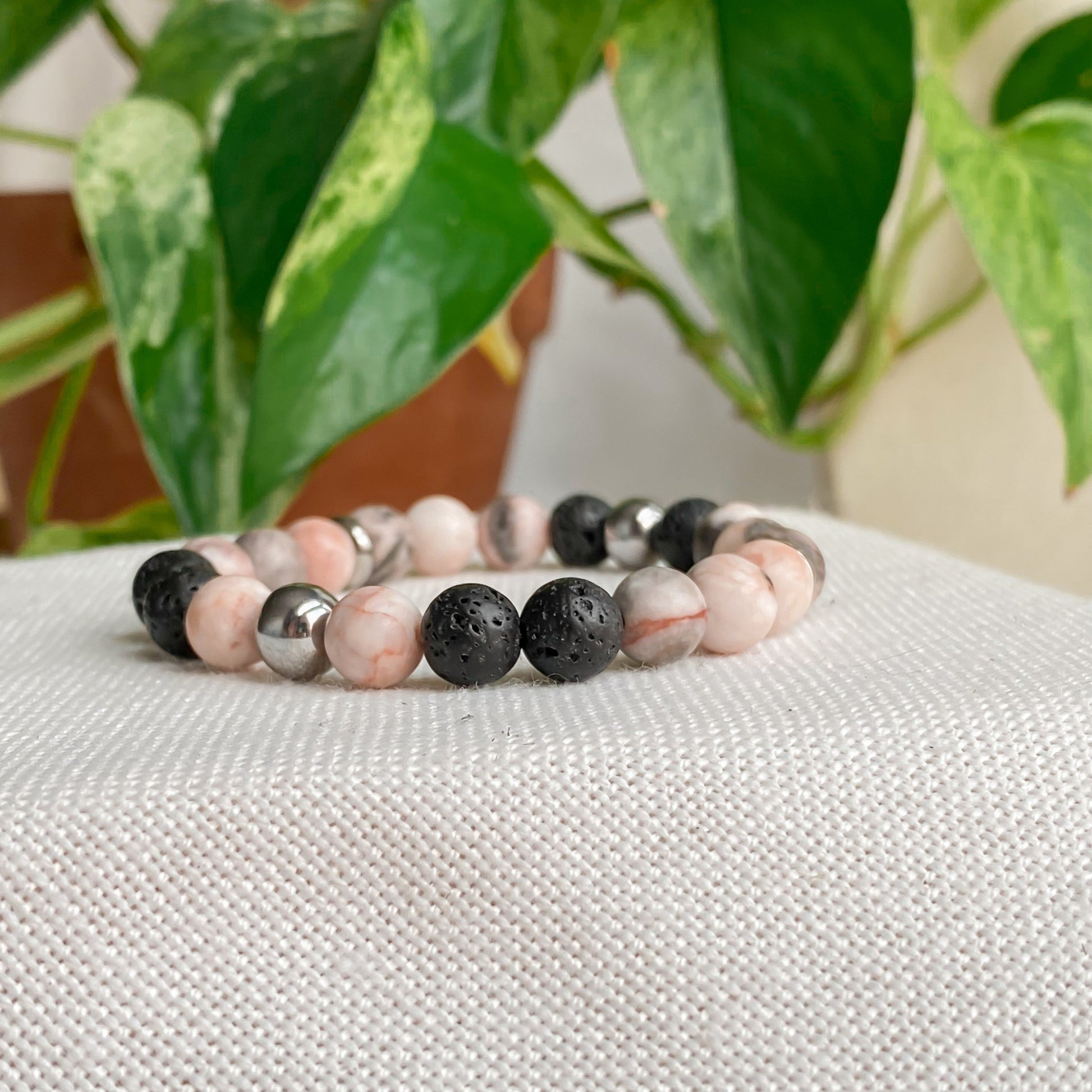 Bracelet élastique Jaspe Zébrée Rose avec Hématite et pierres de lave, vue de face, sur fond coton et feuilles, bijou minimaliste en pierres naturelles.