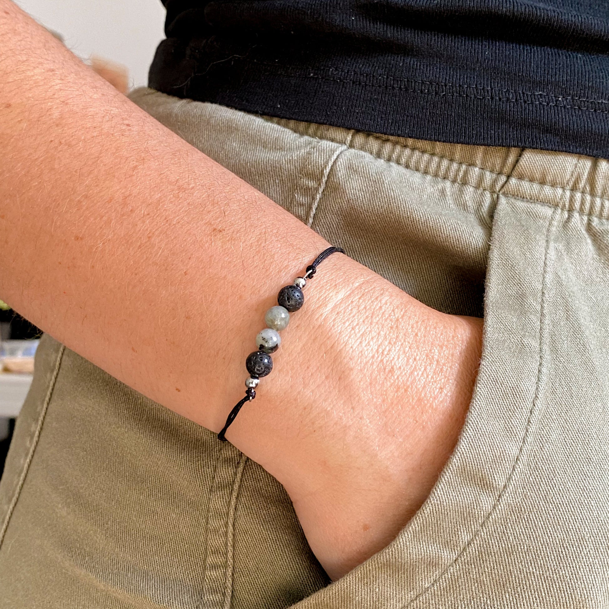 Bracelet minimaliste homme en pierre de lave et labradorite porté au poignet, style décontracté avec pantalon vert et haut noir.