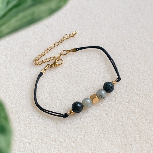 Bracelet NOCTIS pour aromathérapie, cordon noir avec perles de lave poreuses et labradorite aux reflets gris-verts.