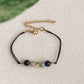 Bracelet cordon ajustable NOCTIS en pierres naturelles, diffuseur d’huiles essentielles, posé à plat avec fermoir doré visible.