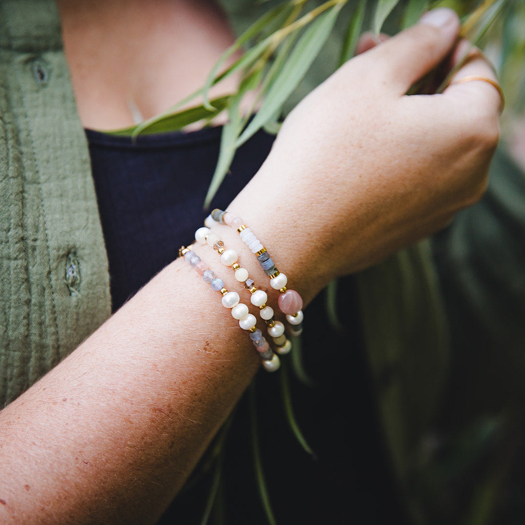 Accumulation de bracelets fins en pierres naturelles et perles d’eau douce dorées, bijou artisanal porté au poignet.