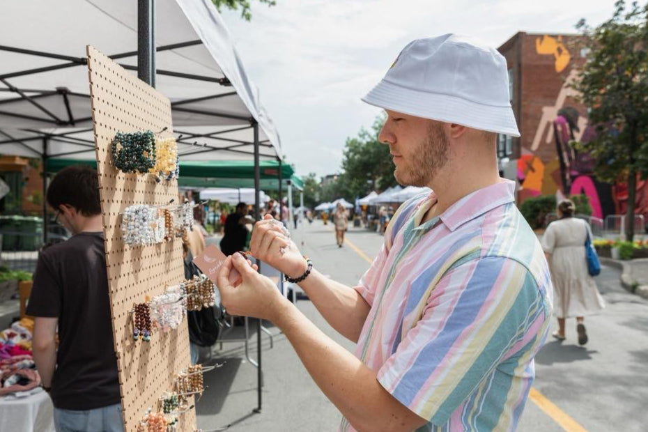 Un visiteur observe les créations de Lunaki Design lors d’un marché d’artisans, attiré par les bijoux en pierres semi-précieuses.