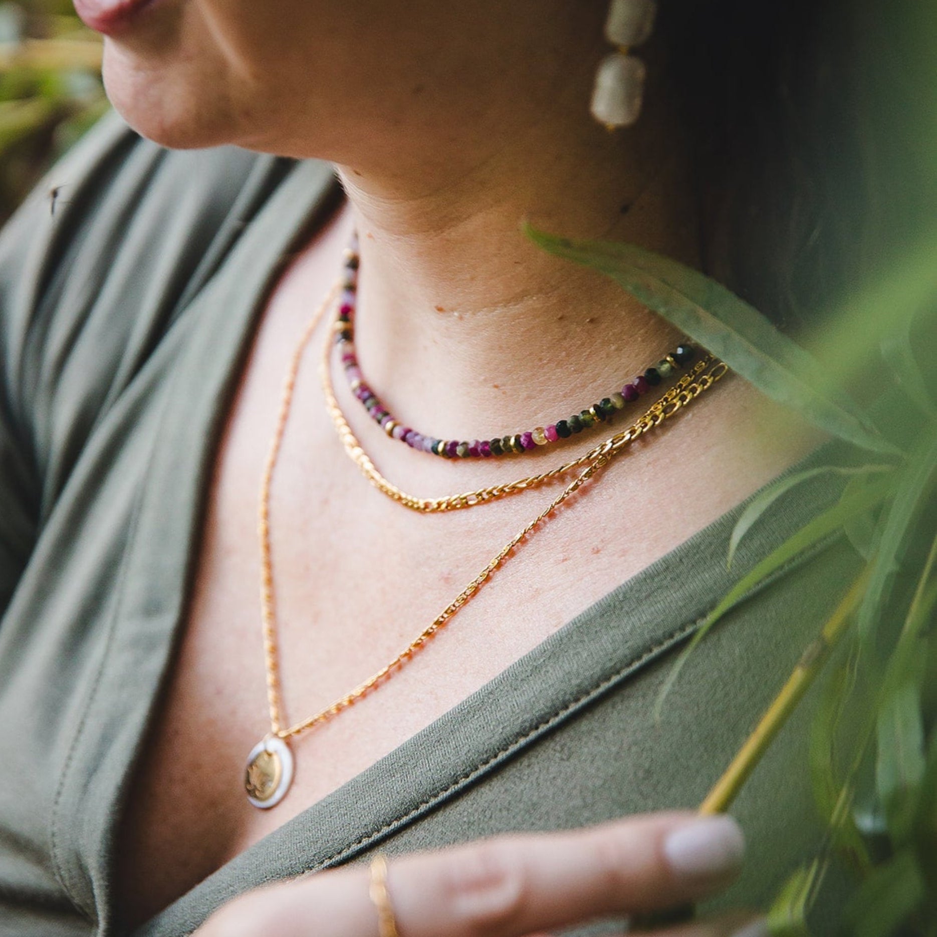 Femme portant le collier Aurora en acier inoxydable doré 18K, superposé avec d’autres colliers et un pendentif, collection Jardin Secret.