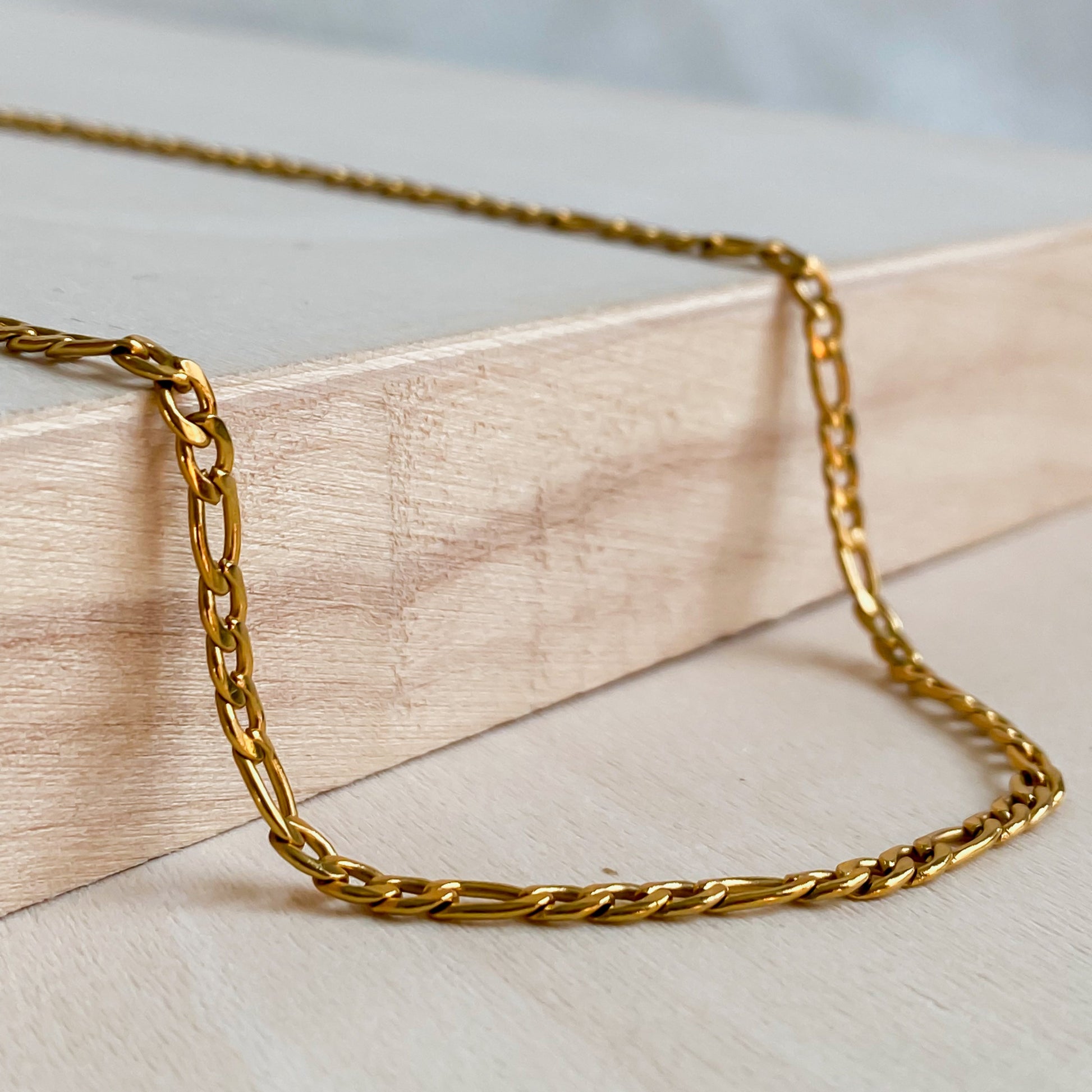 Gros plan du collier Aurora en acier inoxydable 304 doré 18K, maillons fins et délicats sur bois clair.