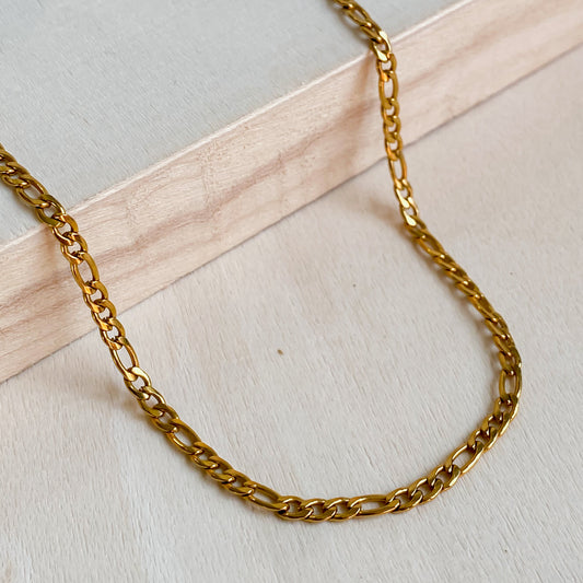 Gros plan du collier Aurora en acier inoxydable doré 18K posé sur une surface en bois clair, mettant en valeur ses maillons fins.