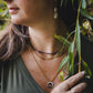 Gros plan sur le collier Aurora en acier inoxydable doré 18K, superposé avec un collier de pierres naturelles et un pendentif doré, look bohème chic.