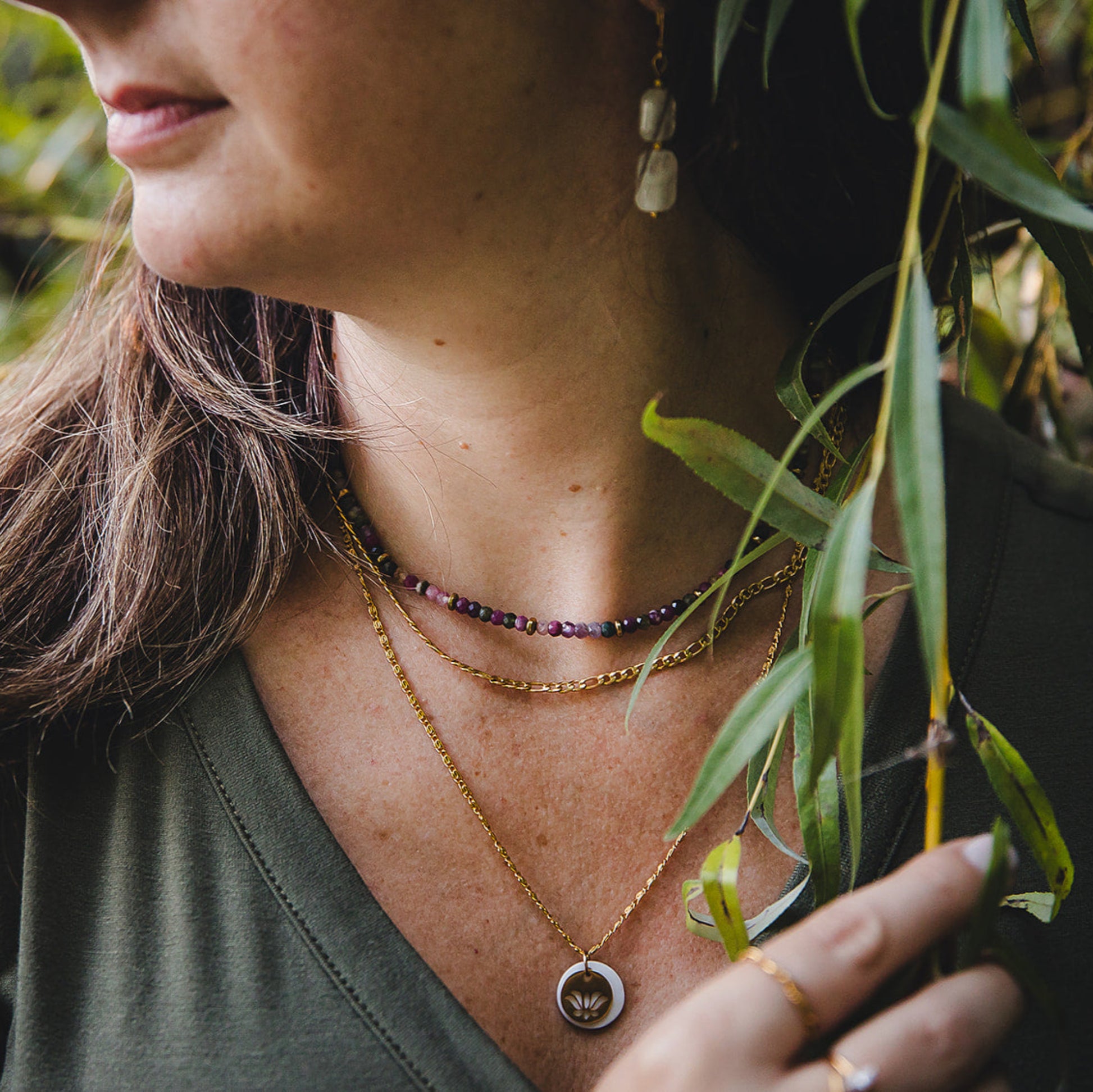 Gros plan sur le collier Aurora en acier inoxydable doré 18K, superposé avec un collier de pierres naturelles et un pendentif doré, look bohème chic.