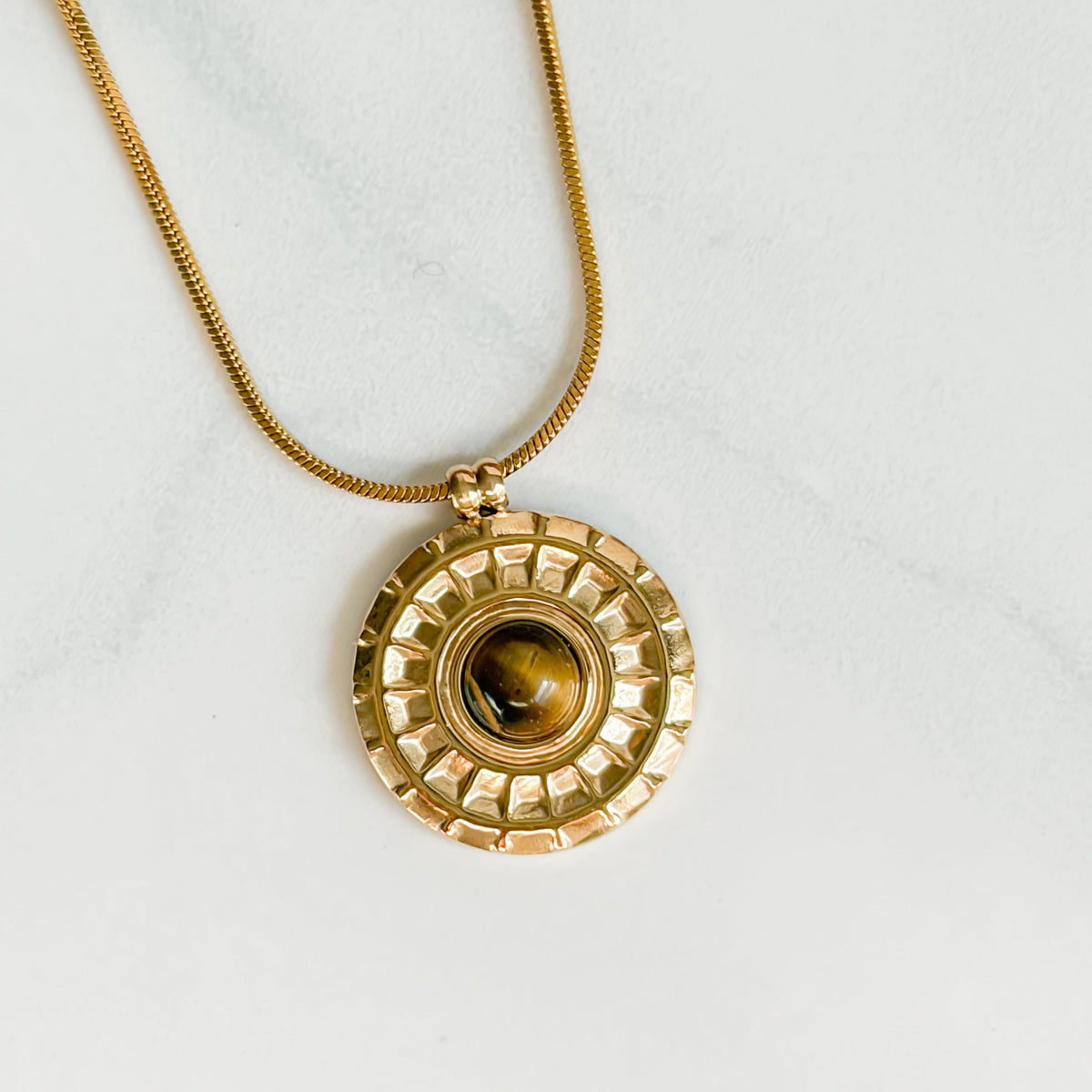 Gros plan du pendentif doré et de l’œil de tigre du collier Bahia