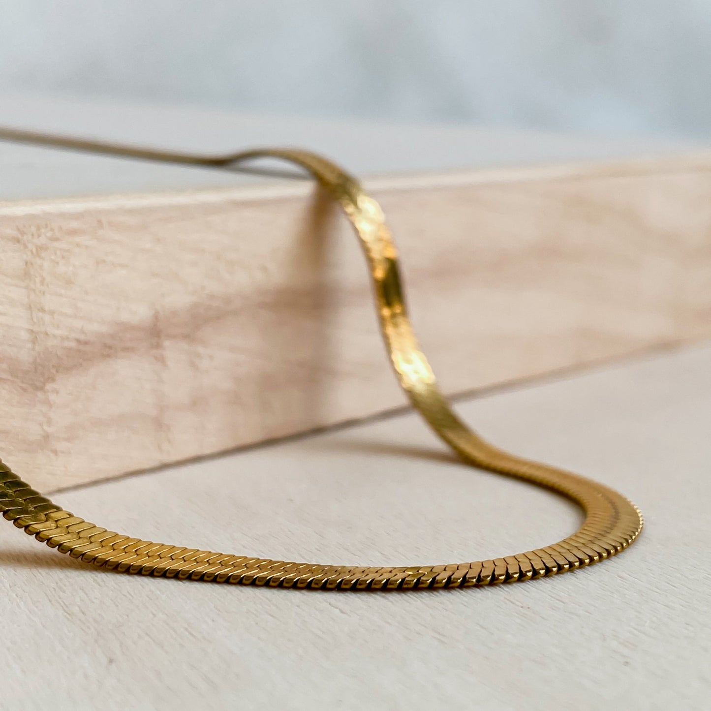 Gros plan sur le collier Cléopâtre doré en maille serpent 18K PVD posé sur bois