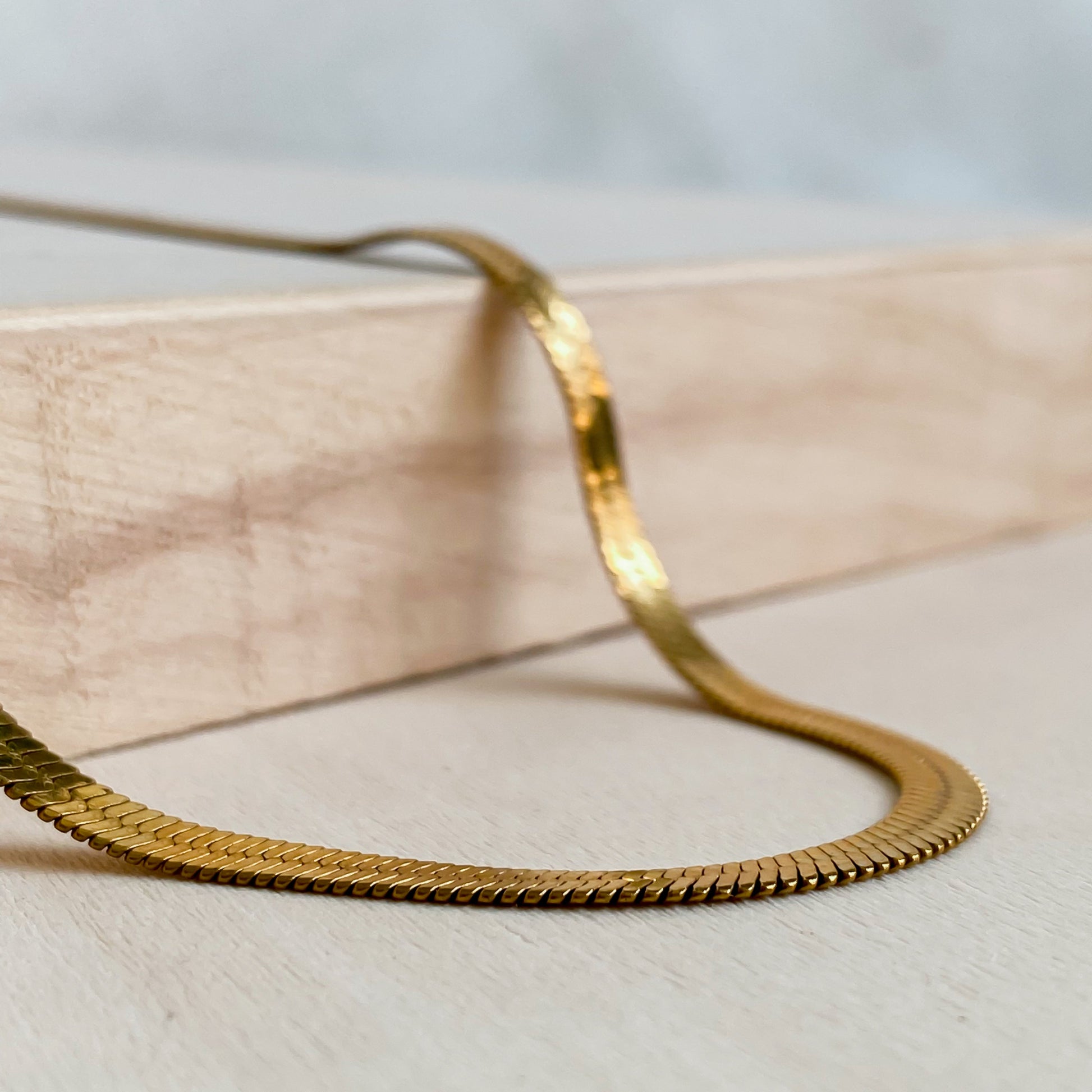 Gros plan sur le collier Cléopâtre doré en maille serpent 18K PVD posé sur bois