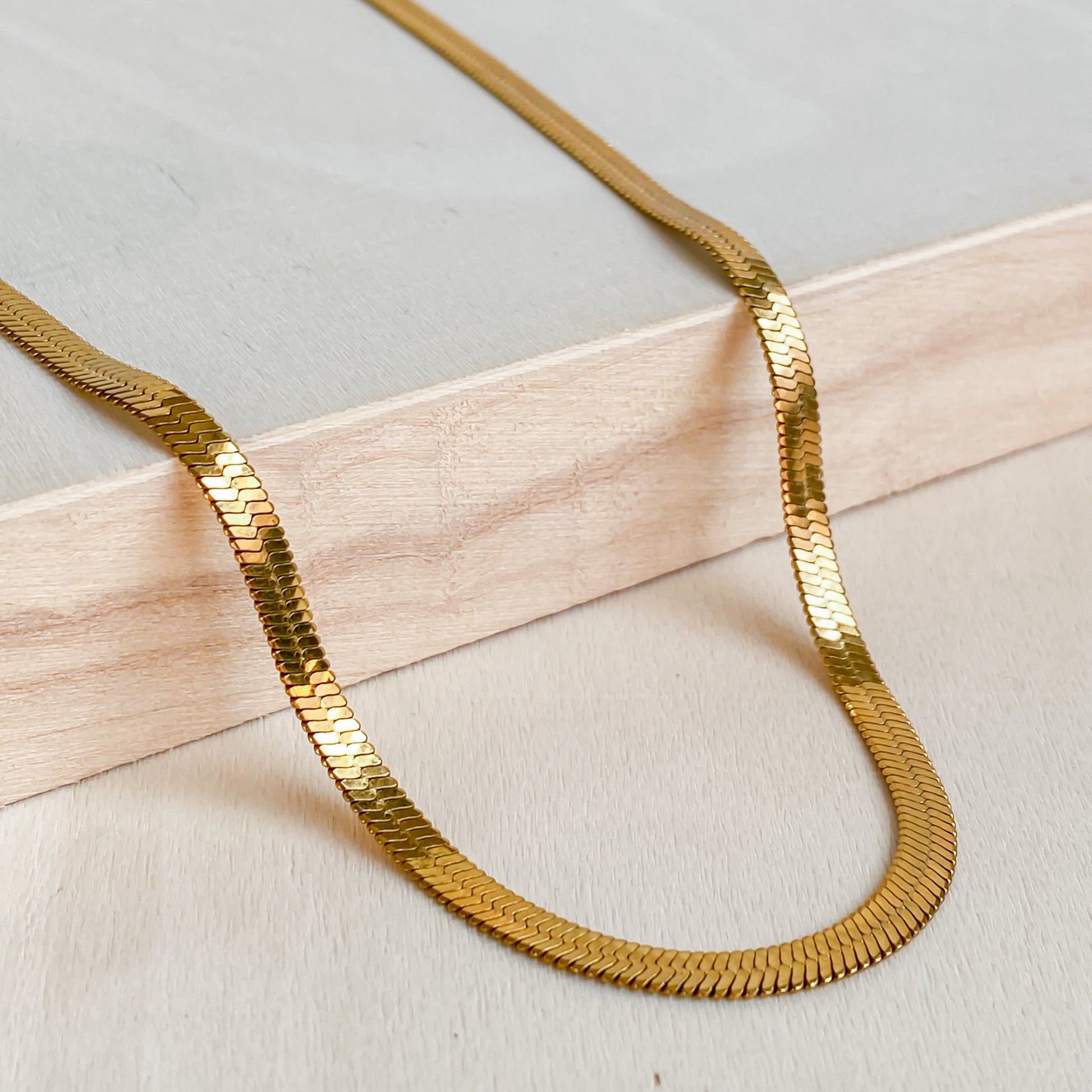 Collier ras de cou Cléopâtre doré en acier inoxydable 18K de Lunaki Design, posé sur bois
