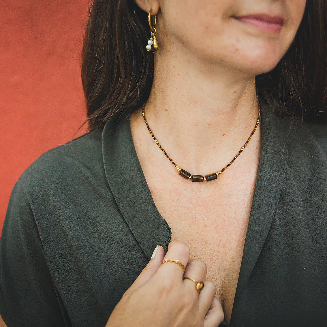 Collier Dune en œil de tigre porté devant un mur terracotta