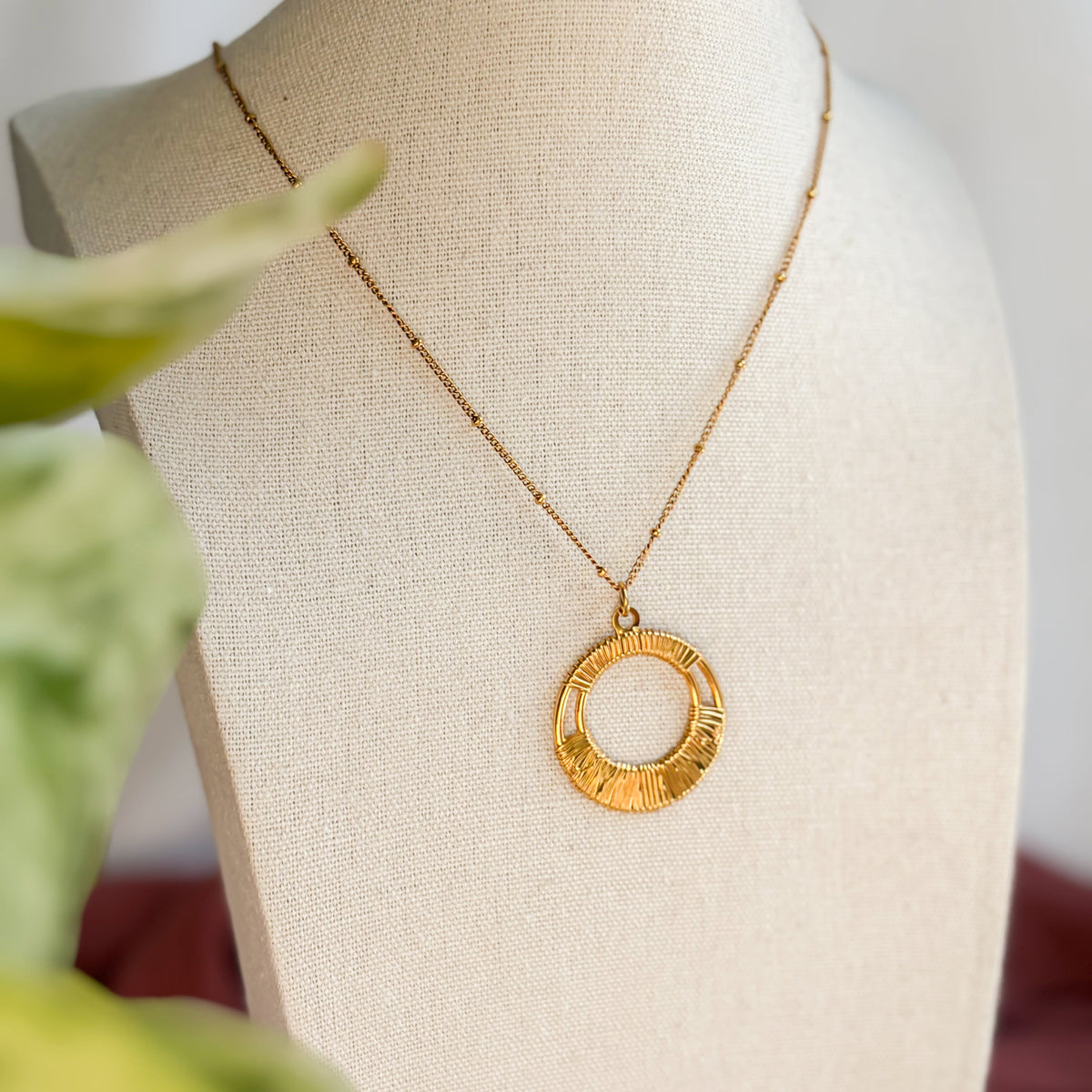 Collier Escale doré à pendentif rond présenté sur un buste
