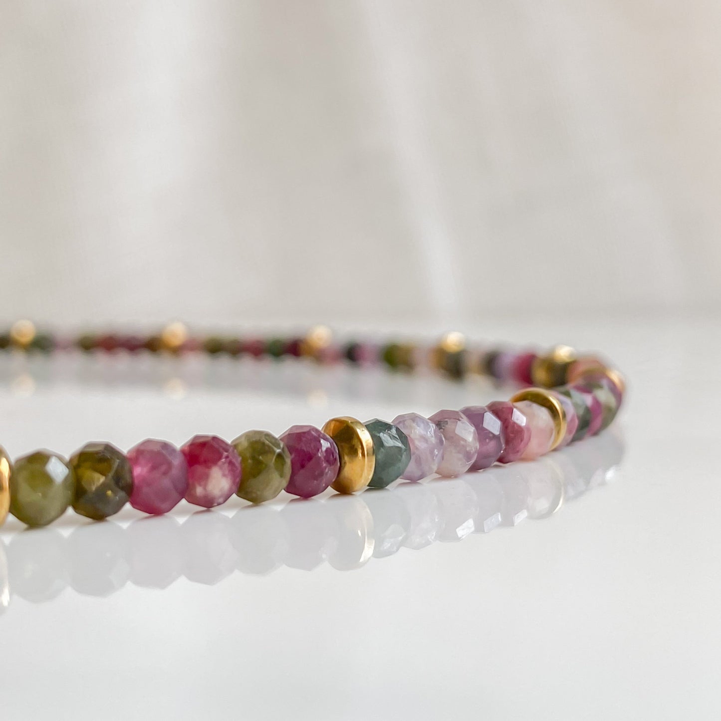 Gros plan du collier Iris, pierres naturelles de tourmaline facettées et intercalaires en hématite dorée, fabrication artisanale.