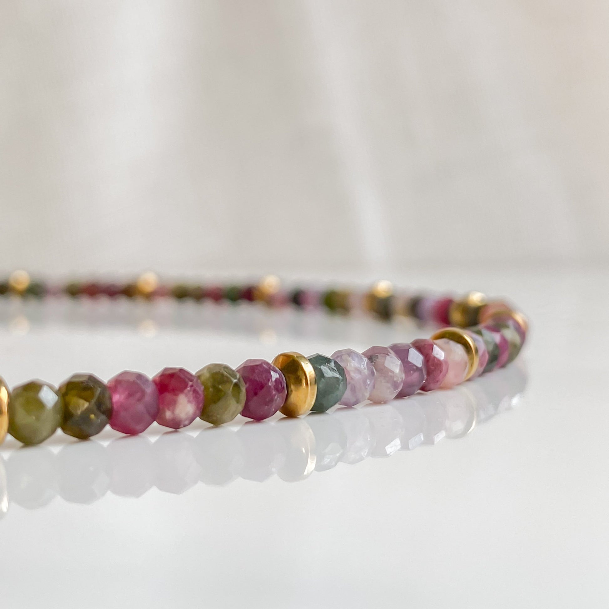 Gros plan du collier Iris, pierres naturelles de tourmaline facettées et intercalaires en hématite dorée, fabrication artisanale.