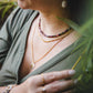 Collier Iris en tourmaline naturelle et hématite dorée superposé avec d’autres colliers dorés, porté par une femme en extérieur, création artisanale Lunaki Montréal.