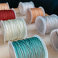 Gros plan sur les différentes couleurs de cordon disponibles pour les bracelets cordon personnalisables, montrant les nuances de noir, blanc, gris clair, vert menthe, champagne, sarcelle, rouge bordeaux, et pêche.