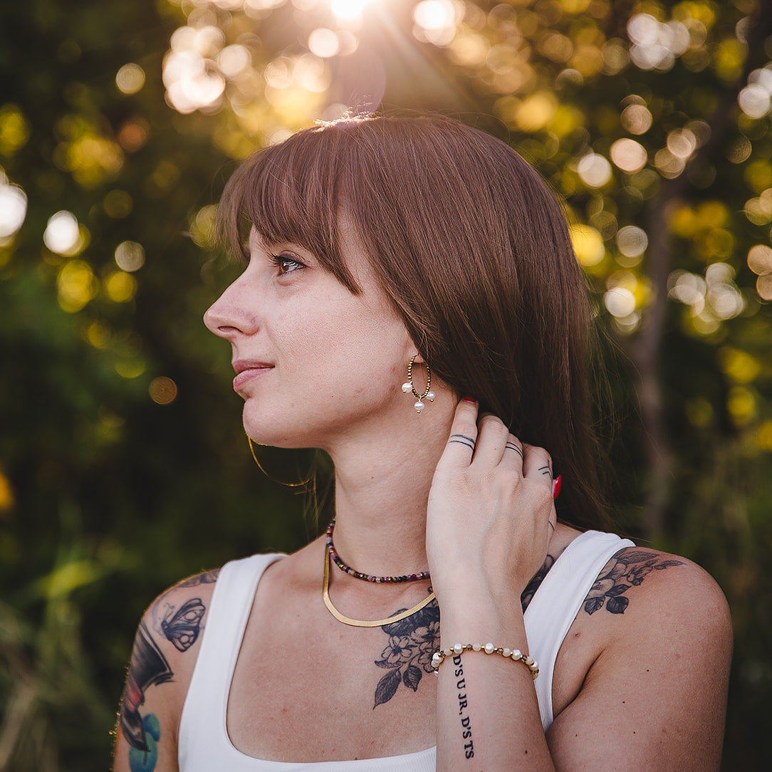 Femme portant les créoles dorées Auréa avec nacres naturelles, bracelet et collier Lunaki Design, en lumière naturelle.