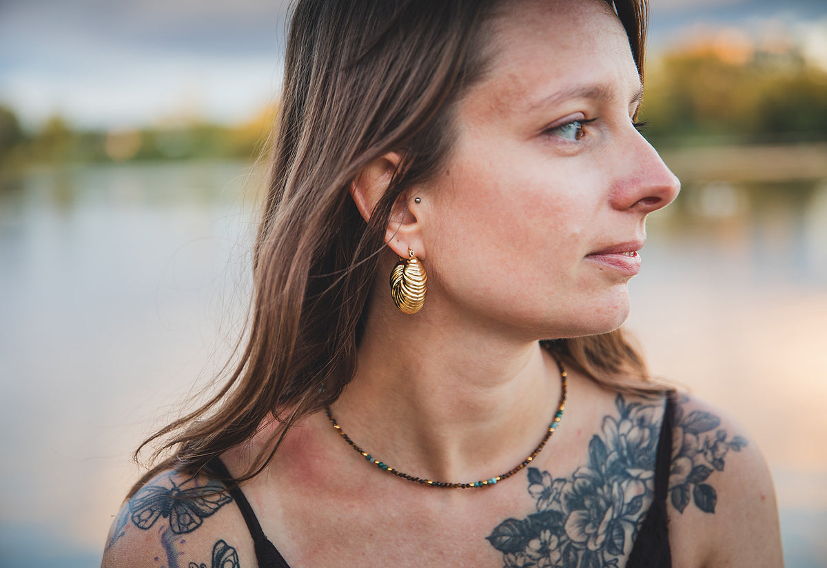 Modèle portant des boucles d’oreilles dorées et un collier en pierres naturelles de la collection Oasis.