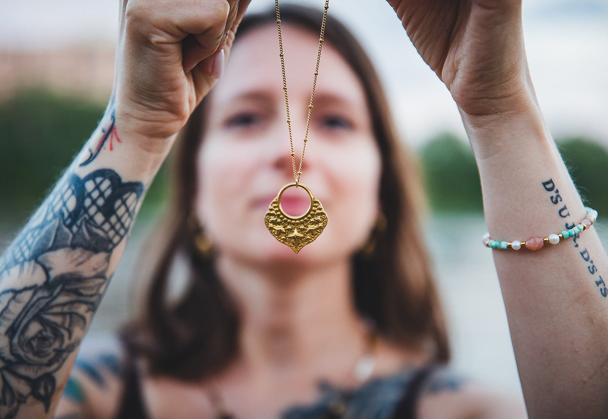 Gros plan sur un collier à pendentif doré et un bracelet en pierres naturelles de la collection Oasis.