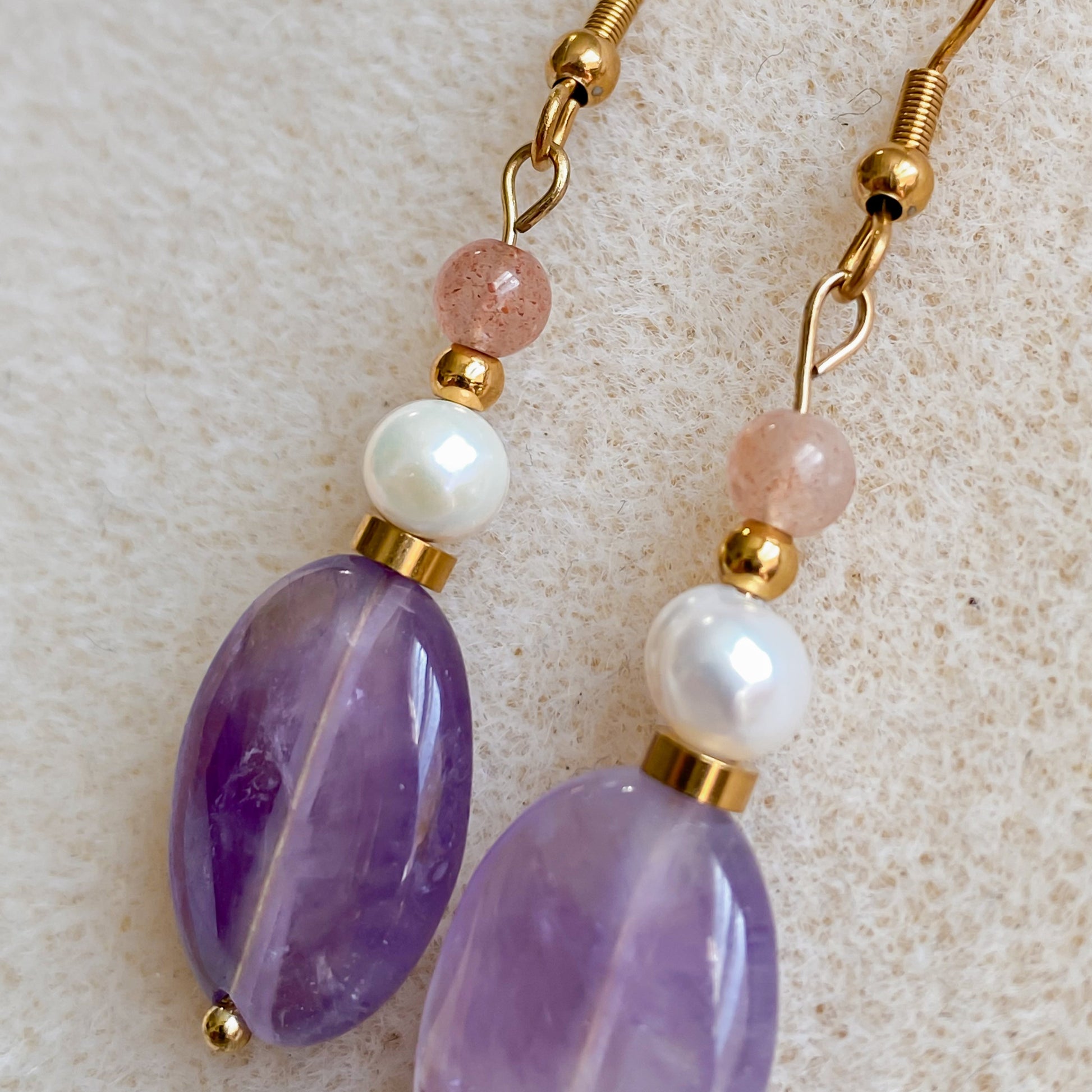 Gros plan sur les boucles d’oreilles Lunara en améthyste ovale, perle d’eau douce et pierre de soleil ronde, montées sur acier inoxydable plaqué or PVD.