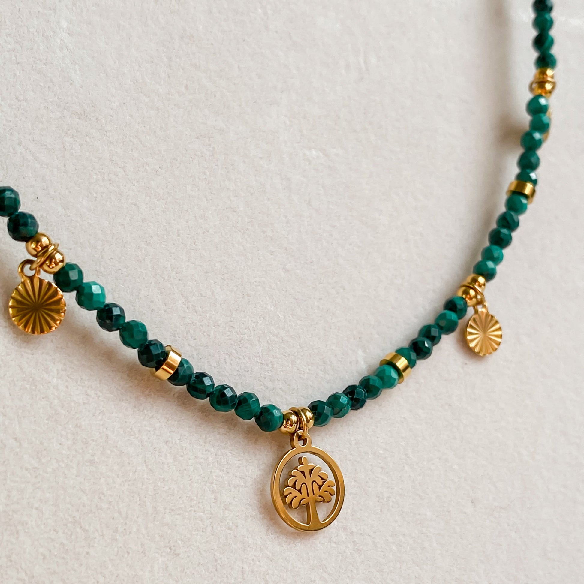 Gros plan sur le pendentif arbre de vie doré du collier Déméter avec perles de malachite facettées.