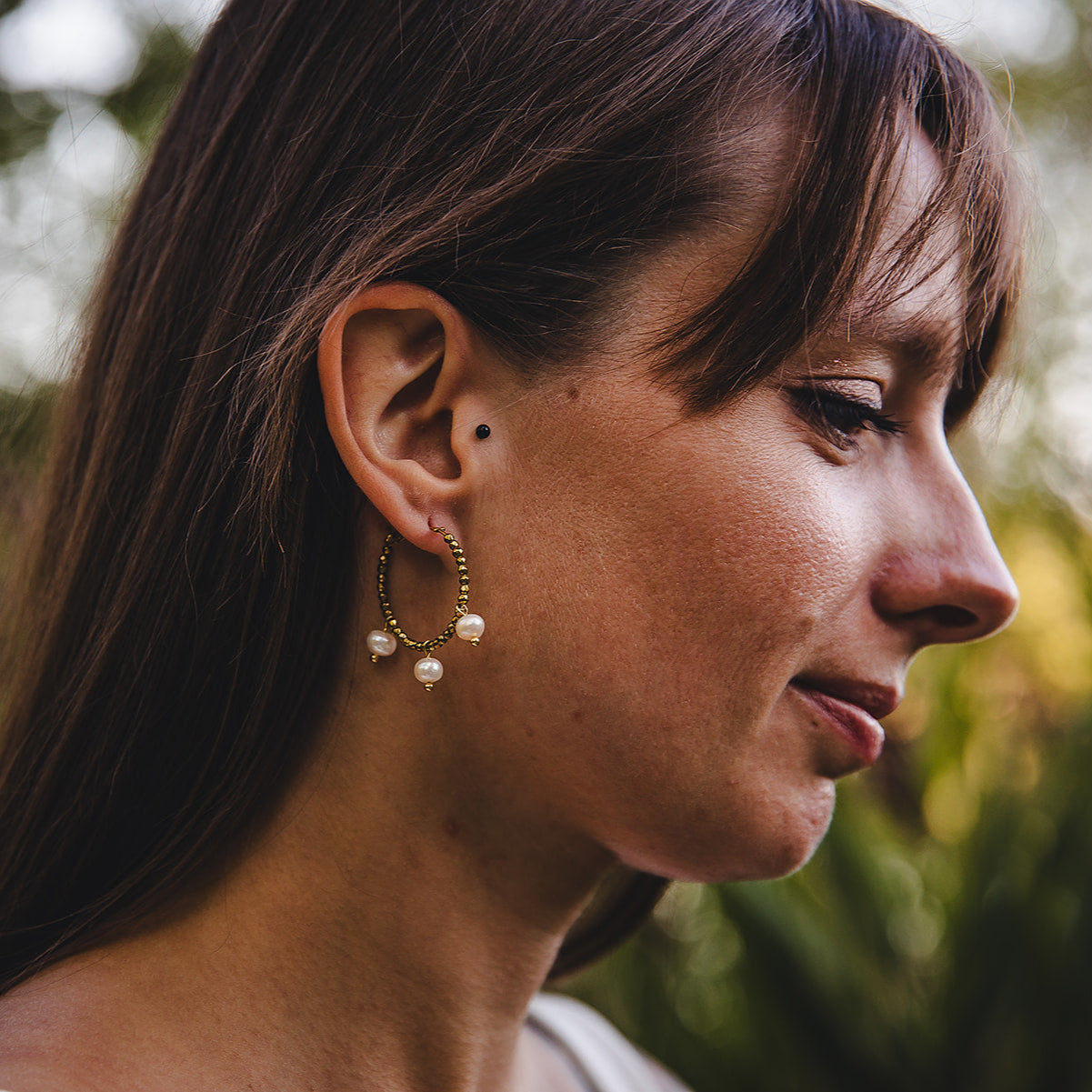 Gros plan sur une femme portant les boucles d’oreilles Auréa, créoles dorées artisanales avec nacres d’eau douce.