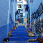 Ruelle et escaliers bleus bordés de boutiques artisanales à Chefchaouen au Maroc.