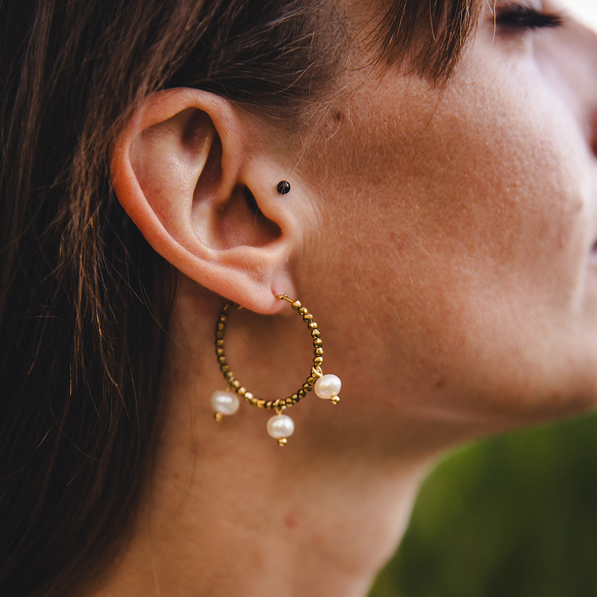 Gros plan d’une oreille portant les créoles Auréa dorées avec nacres suspendues, bijou artisanal lumineux.